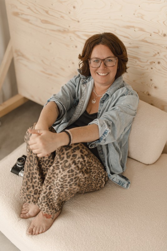 Fotografin sitzt auf einem Sofa und lächelt.